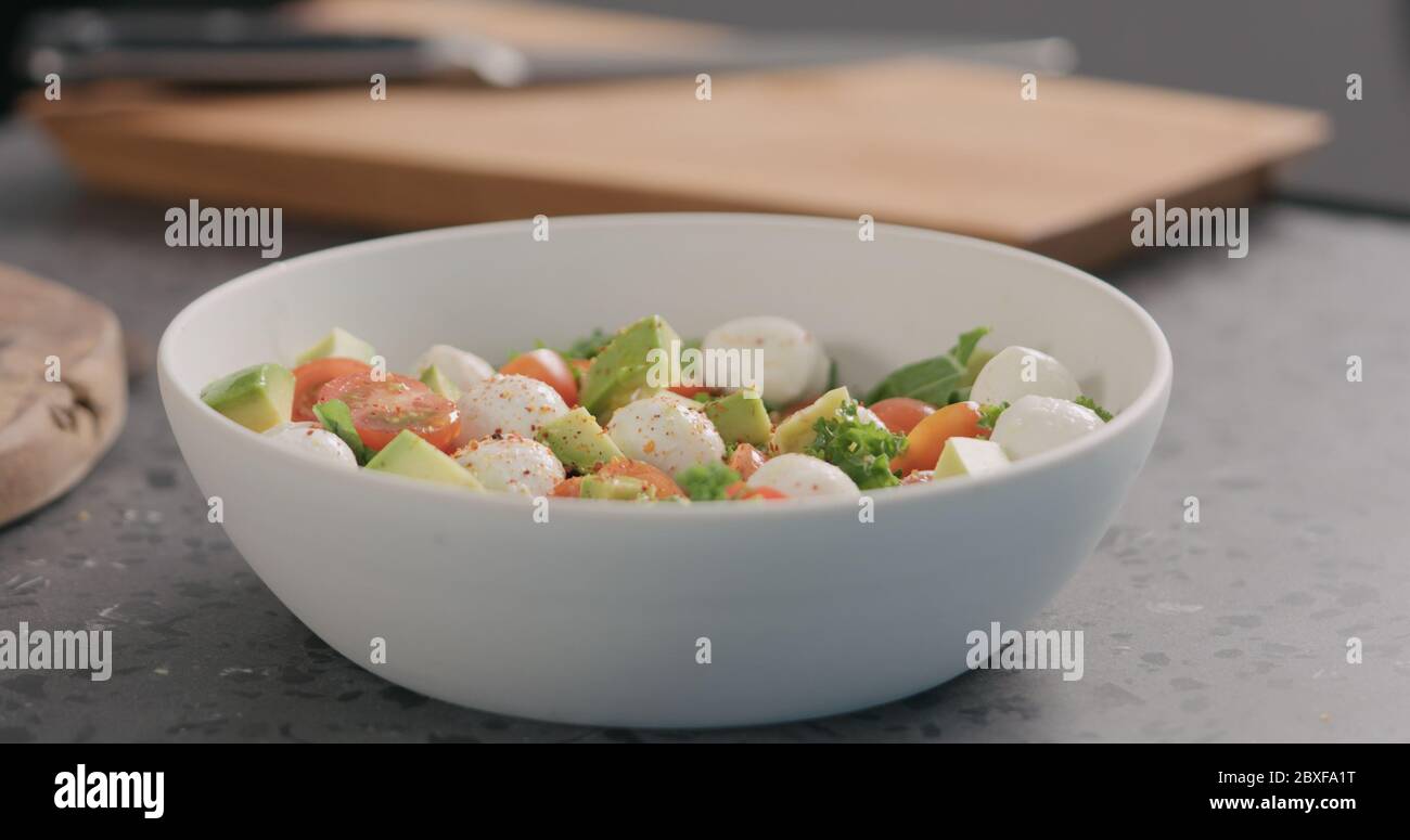 Gewürze in Salat mit Grünkohl, Avocado, Mozzarella und Tomaten in einer weißen Schüssel auf der Küchenarbeitsfläche geben Stockfoto