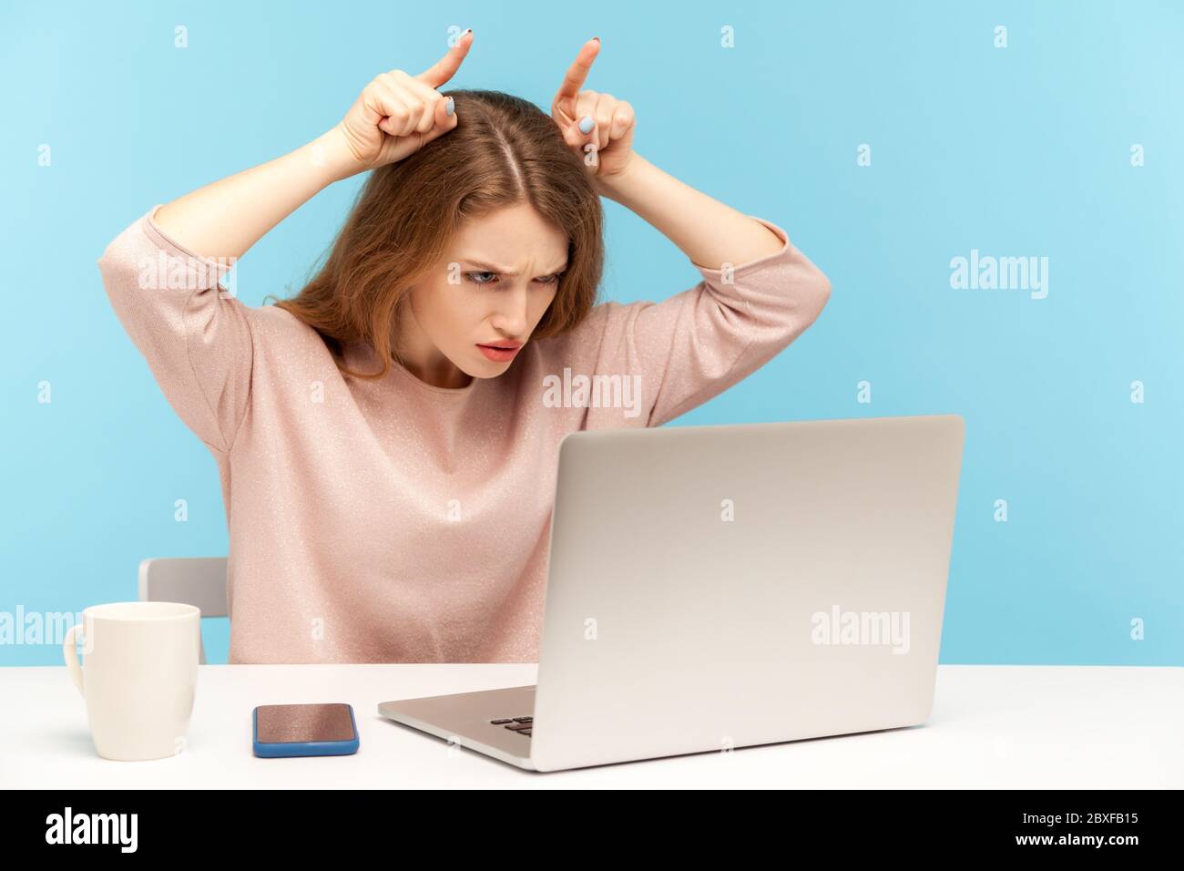 Aggressive junge Frau Mitarbeiter tun Stier Horn Geste und Blick wütend auf Laptop-Bildschirm, Drohung, Wut auszudrücken, während im Gespräch auf Videoanruf. In Stockfoto