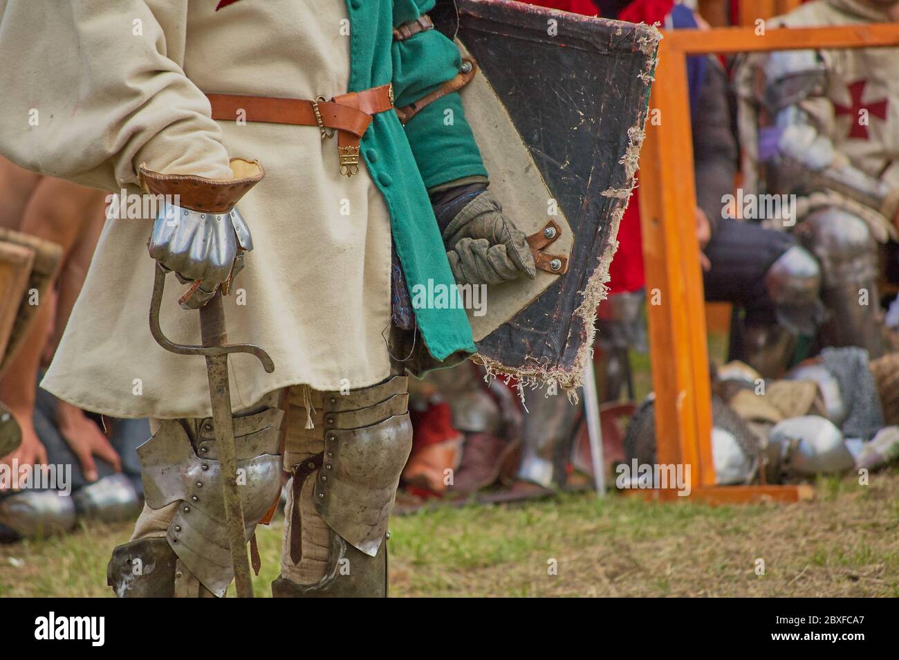 Ein Mann in einem Ritterkostüm, der sich auf ein Schwert stützt und einen beschädigten Schild hält Stockfoto