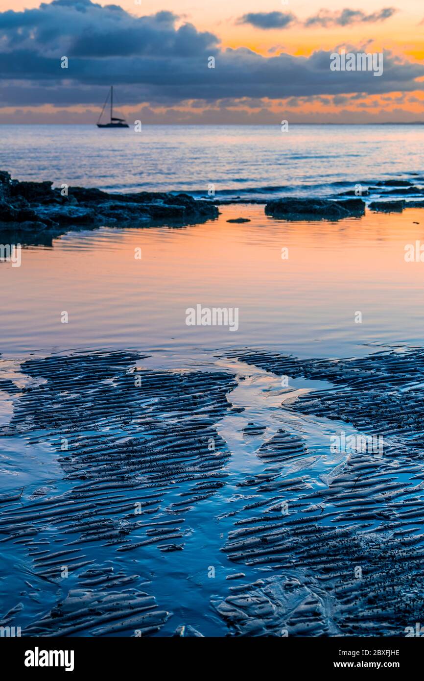 Wellen und Reflexionen auf nassem Strandsand im frühen Morgenlicht Stockfoto