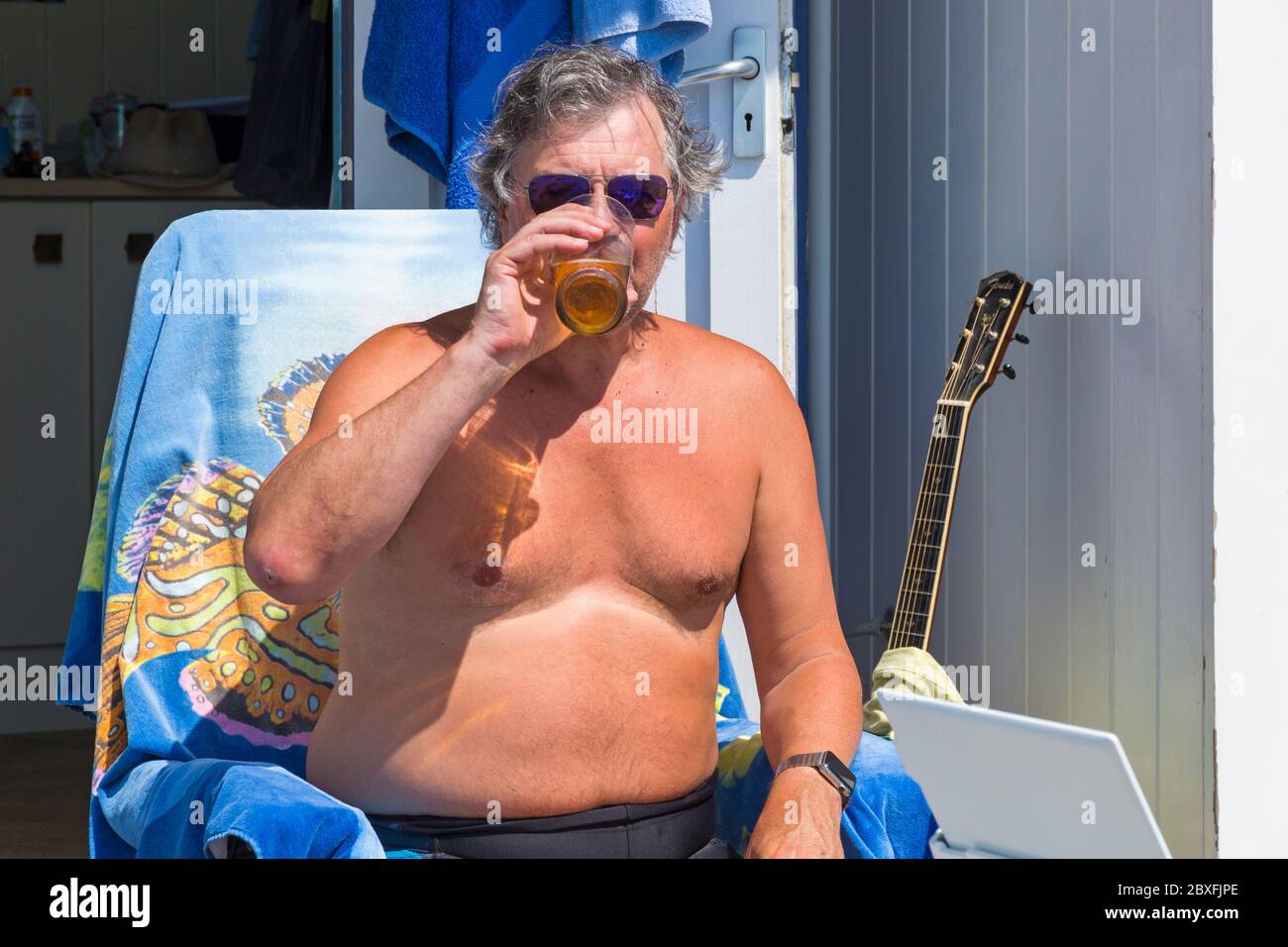 Mann, der im Juni einen Drink genießt, während er die Sonne in seiner Strandhütte in Bournemouth, Dorset UK, genießt Stockfoto