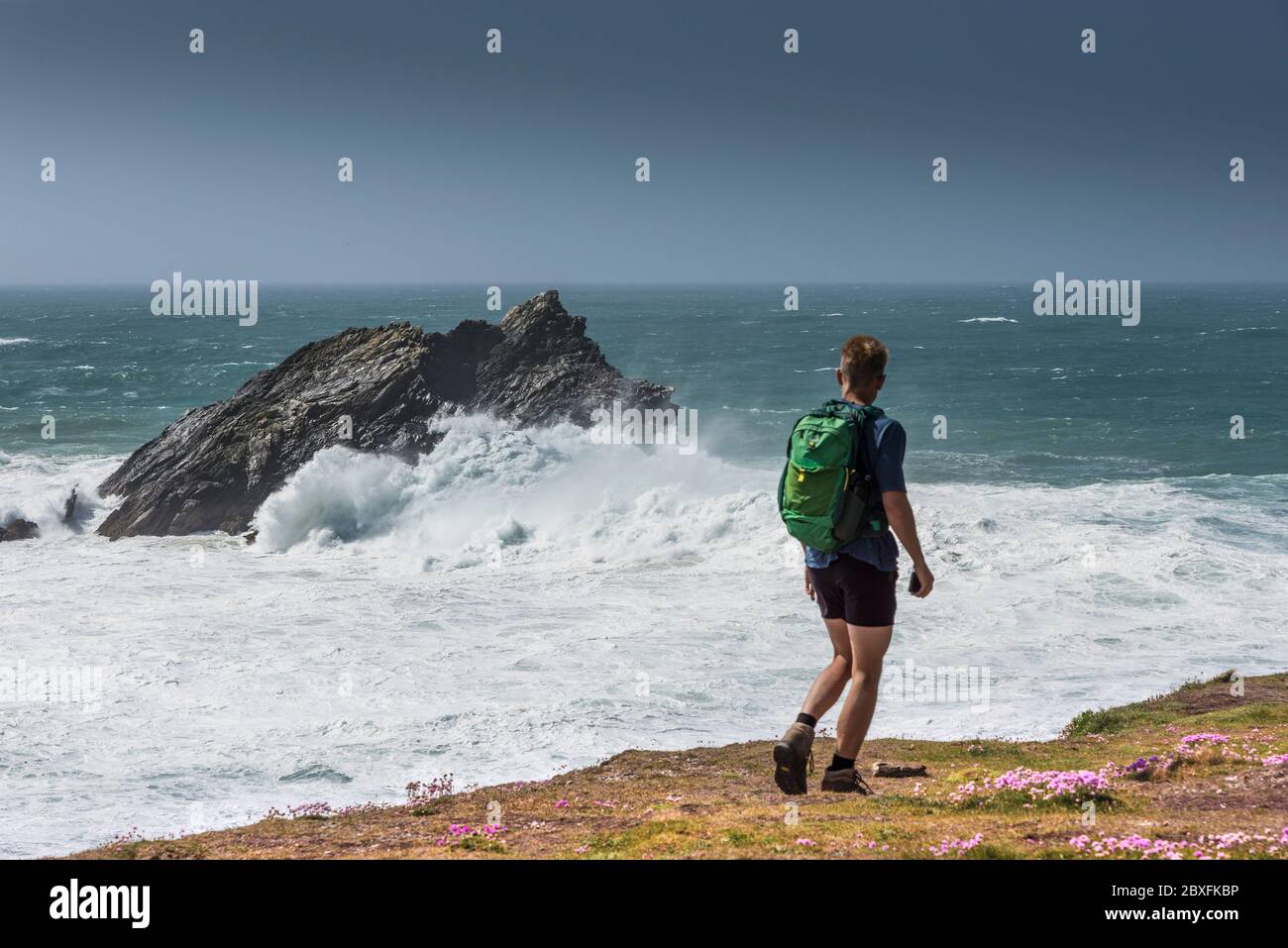 Ein Wanderer beobachtet wilde Wellen, die über Goose Island vor der Küste von Pitch Point East in Newquay in Cornwall schlagen. Stockfoto