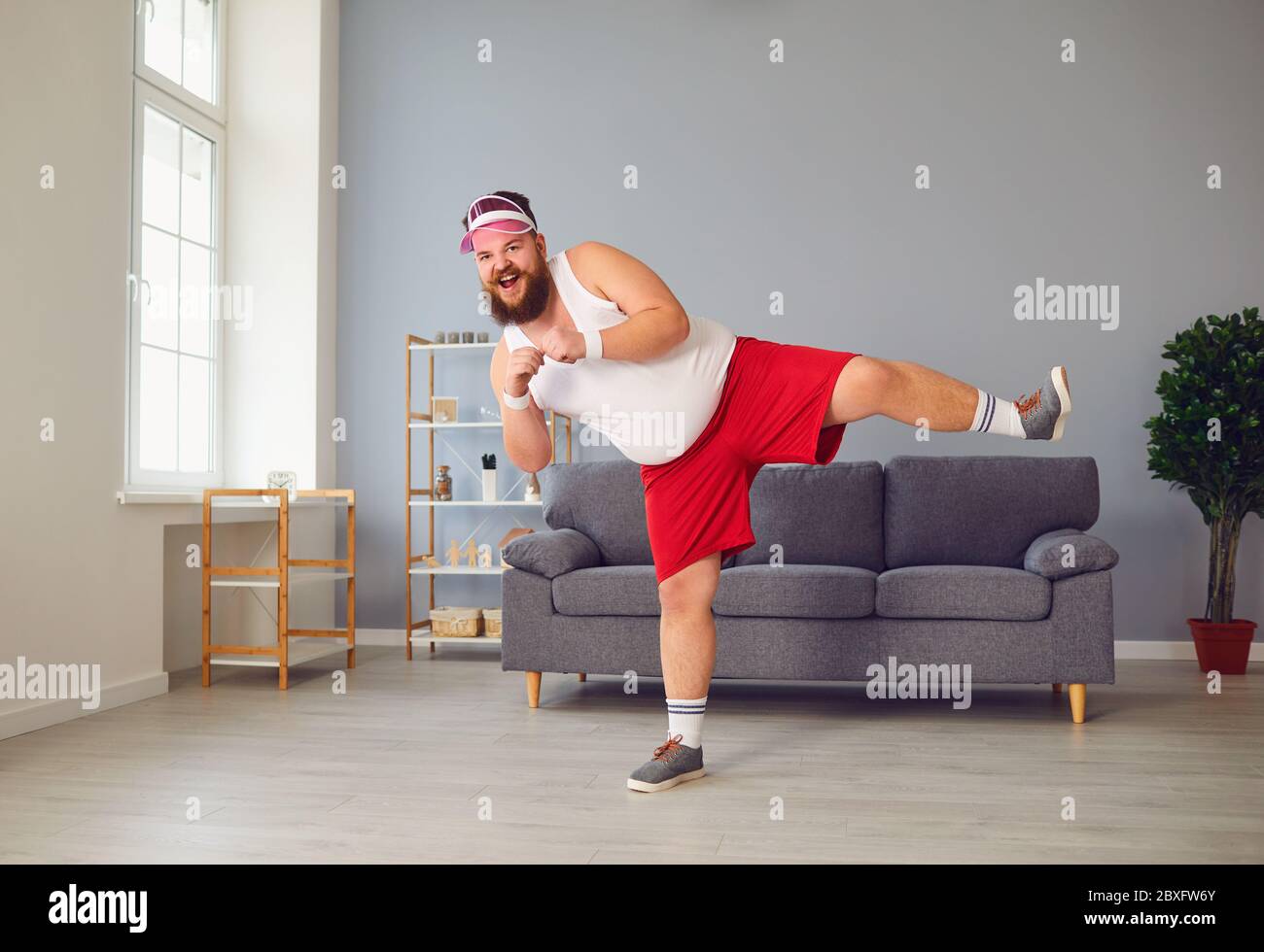 Lustiger fetter Mann in roten Shorts und weißem T-Shirt lächelnd Übungen im Raum machen Stockfoto