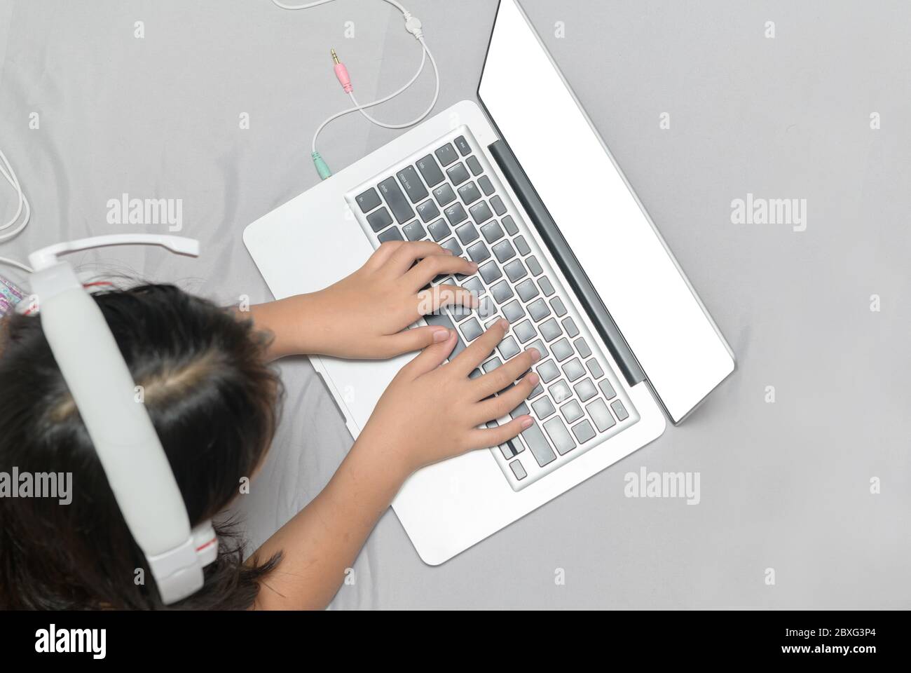 Mädchen liegen und tragen Kopfhörer, um online von einem Laptop auf dem Bett zu Hause lernen. Top-Ansicht und weißen Bildschirm. Neues normales Konzept Stockfoto