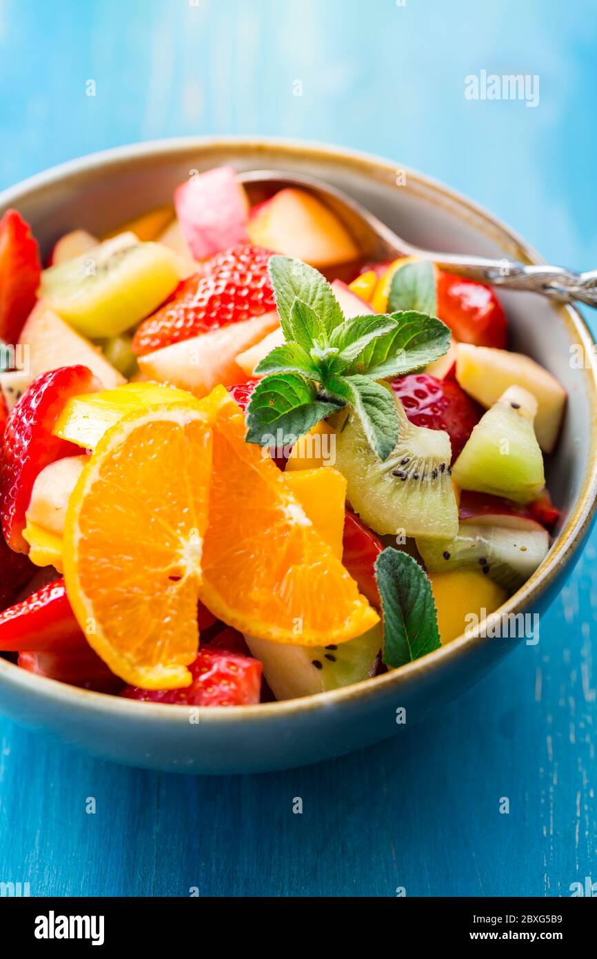 Frischer Obstsalat voller Vitamine für den Sommer mit Minze auf blauem Hintergrund Stockfoto