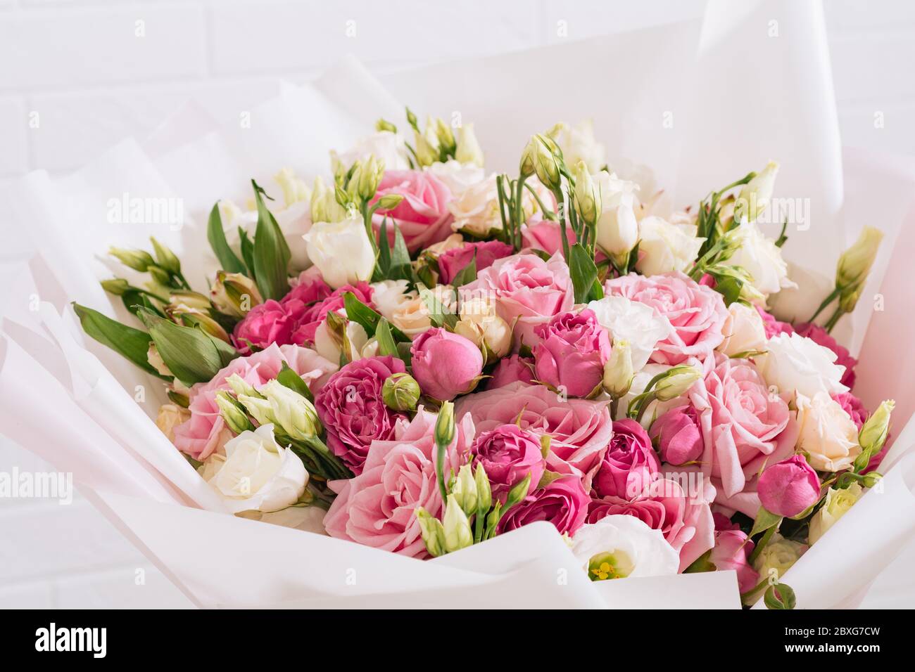 Großer Strauß von schönen und hellen weiß-rosa Rosen und eustoma in rosa Verpackung auf einem weißen Wandhintergrund Stockfoto