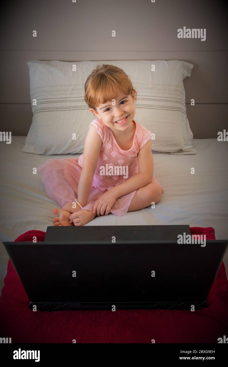 Porträt eines lächelnden Mädchens, das mit einem Laptop auf einem Bett sitzt Stockfoto