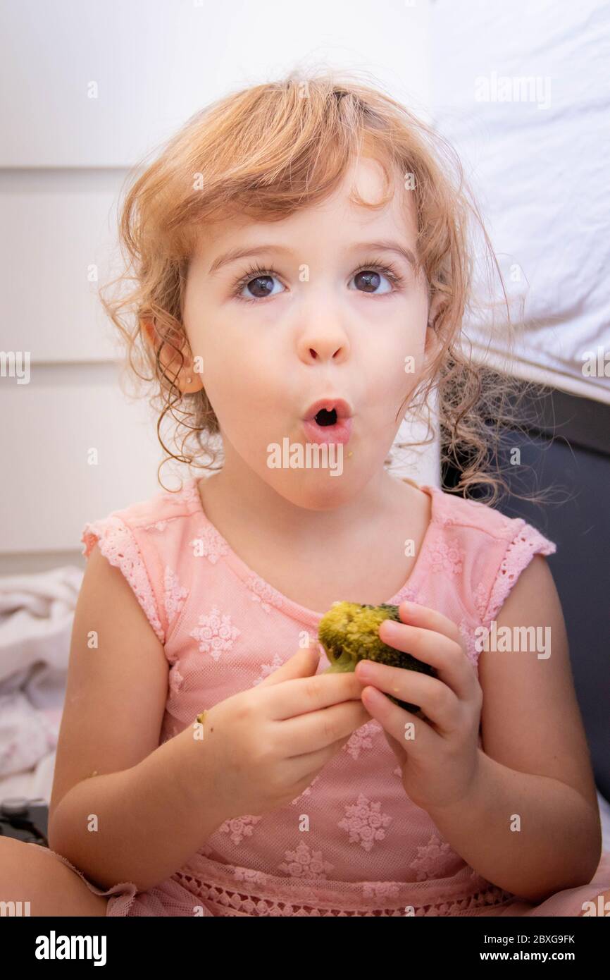 Porträt eines Mädchens, das Brokkoli isst und lustige Gesichter zieht Stockfoto