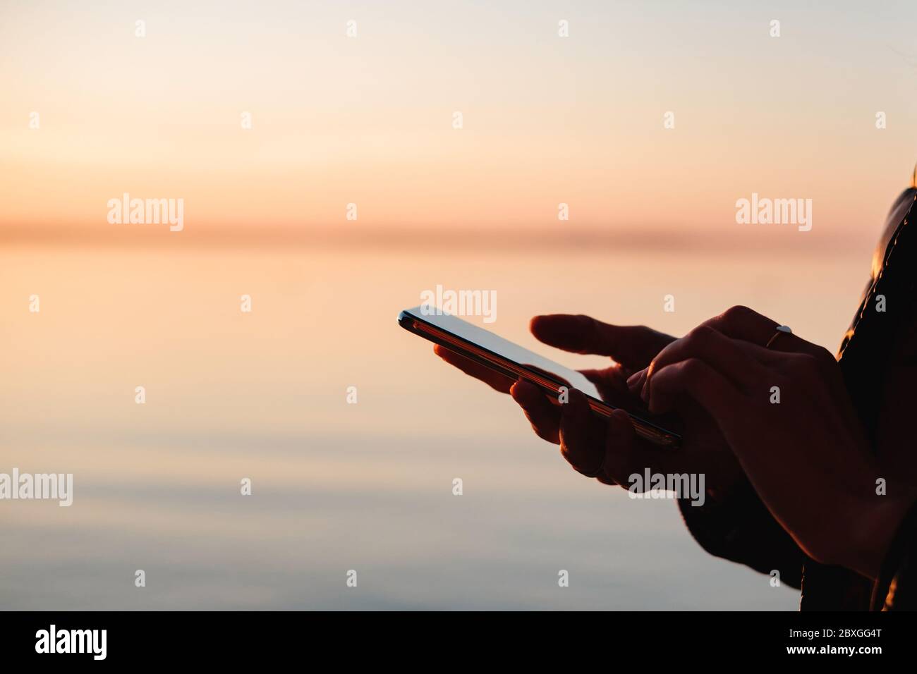 Nahaufnahme einer Frau, die ein Mobiltelefon auf dem Seeweg bei Sonnenuntergang, Weißrussland Stockfoto
