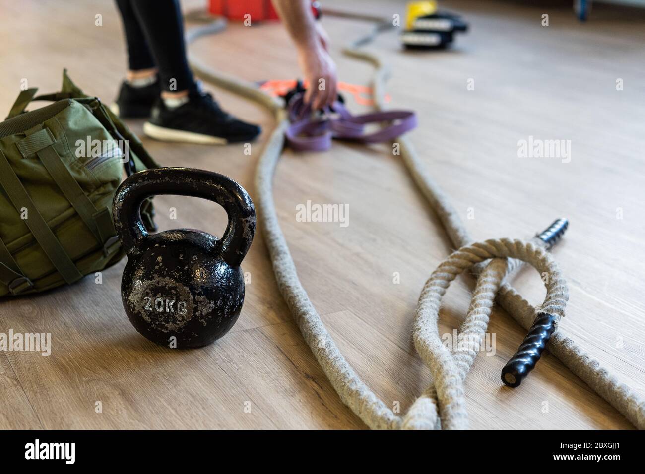 Vorbereitung der Fitnessgeräte für Boot Camp und trainieren mit Wasserkocher Glocke, Seil, Sandsack in Turnhalle auf dem Boden. Beine des Instruktors im Hintergrund. Stockfoto