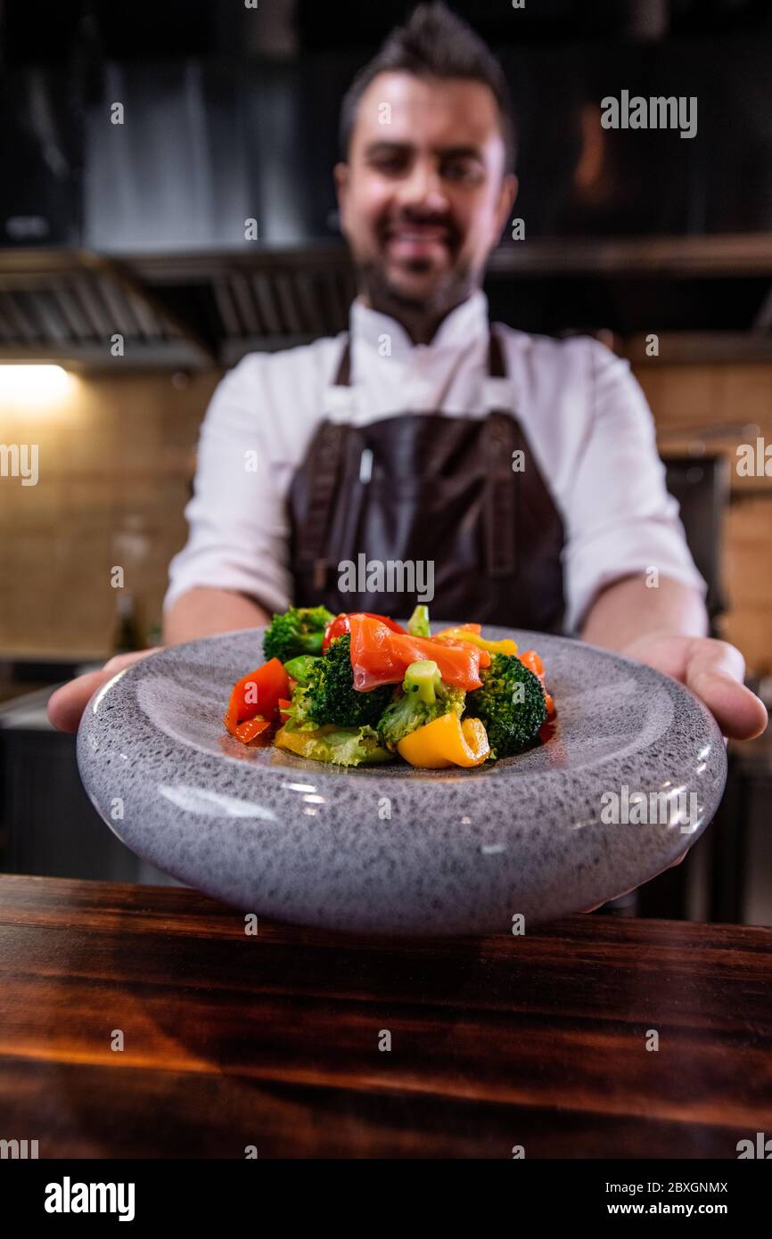 Nahaufnahme des Restaurantkochs, der Salatgerichte auf einem runden Teller über dem Tresen serviert Stockfoto
