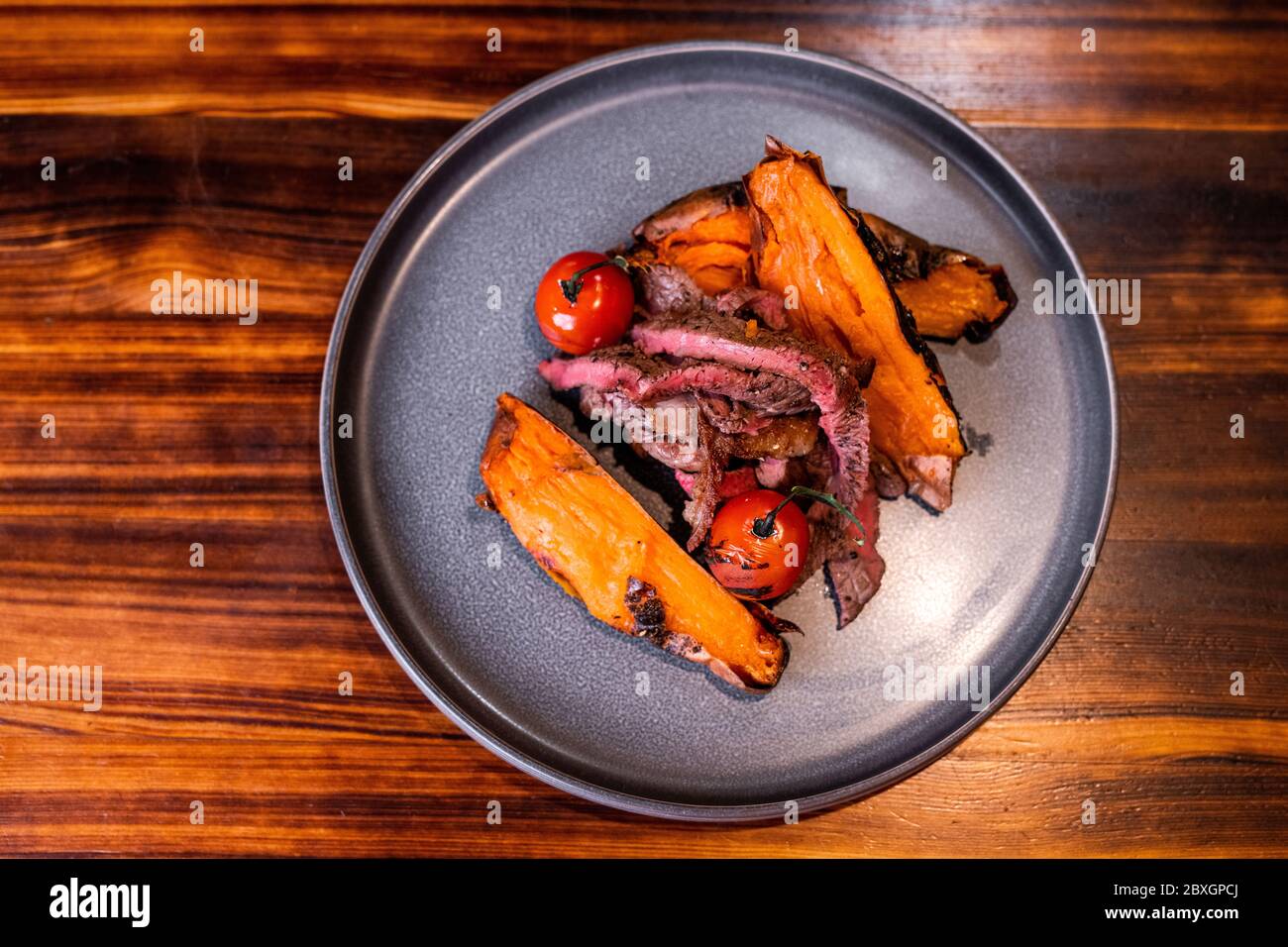Schönes Fleischgericht mit Tomaten und Süßkartoffeln auf dem Teller, Speisenpräsentation Stockfoto