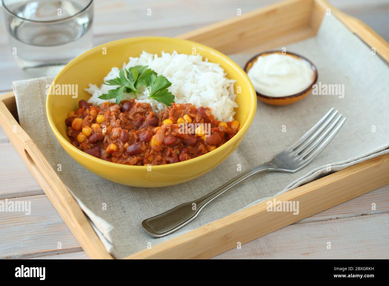 Chili con Carne mit langkörnigem Reis, verziert mit einem Blatt Petersilie und serviert mit saurer Sahne Stockfoto