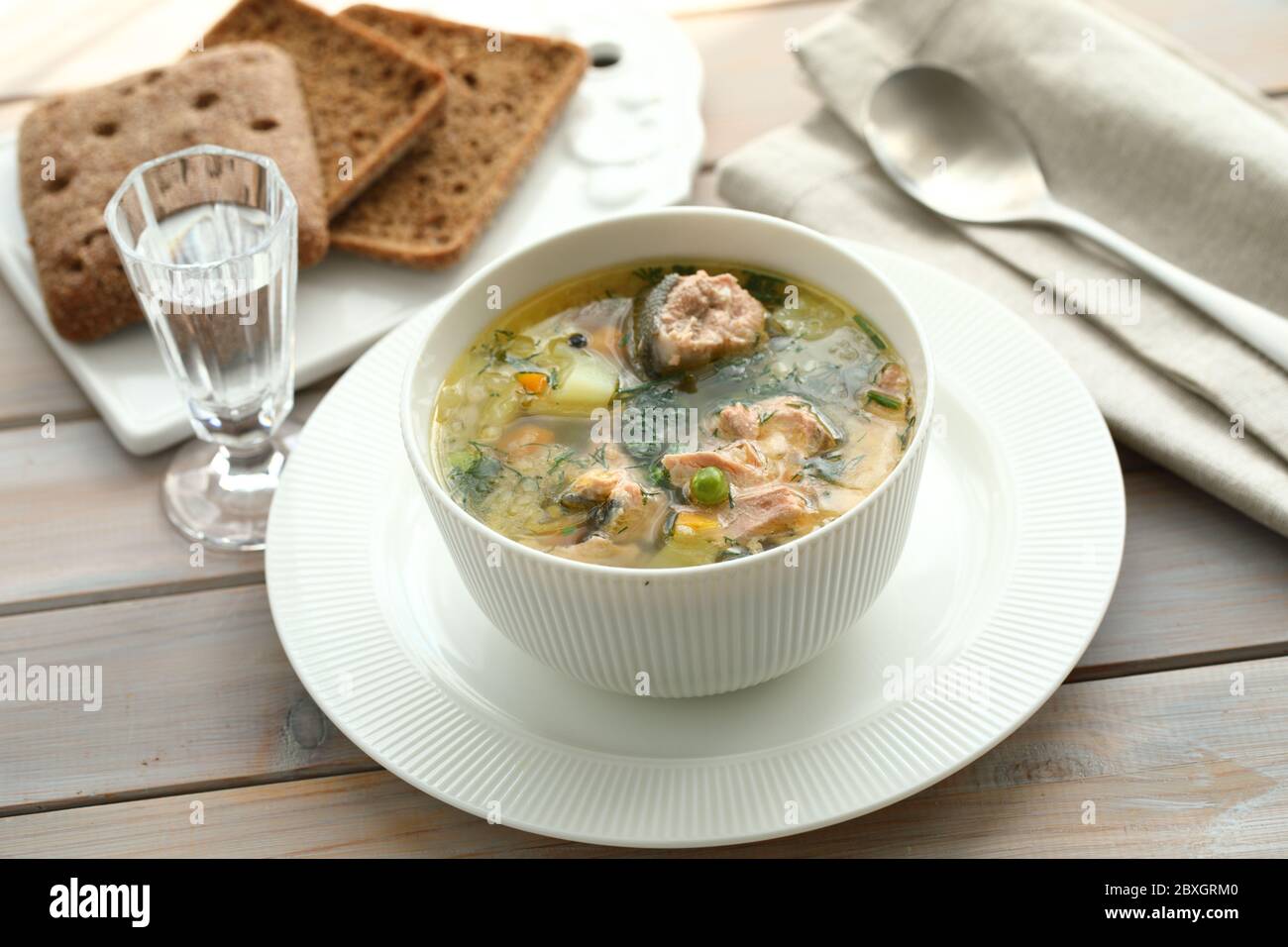 Lachssuppe in einer weißen Schüssel mit Roggenbrot und einem Schuss Wodka serviert Stockfoto