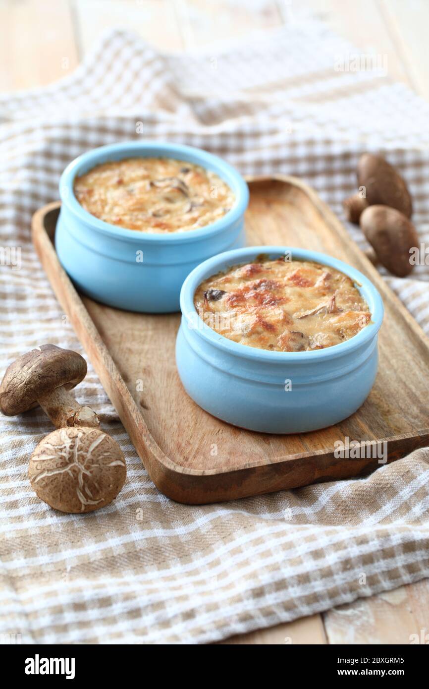 Pilzgratins in zwei blauen Töpfen auf einem Holztablett Stockfoto