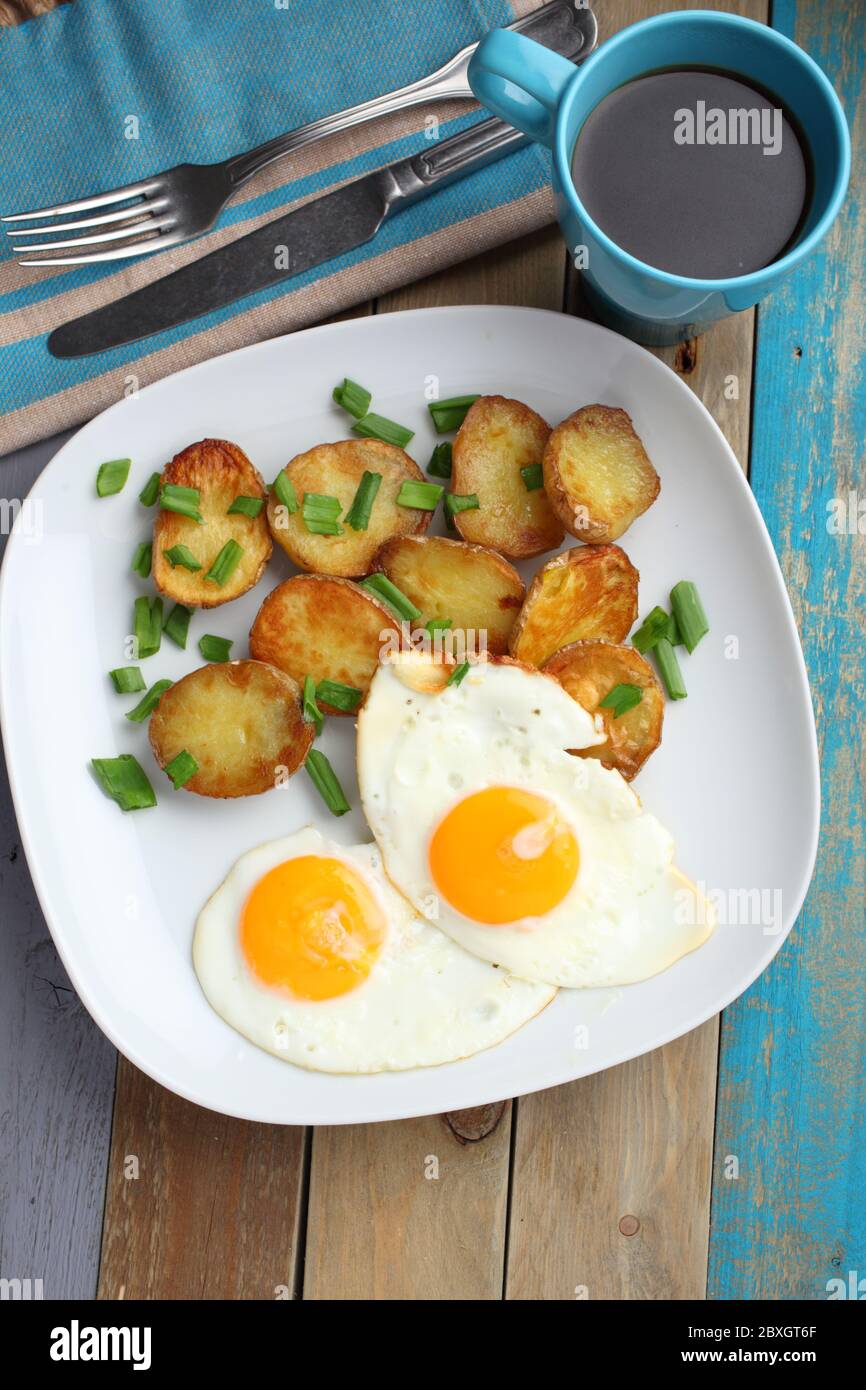 Spiegeleier mit gerösteten Kartoffeln und grüne Zwiebel auf einem rustikalen Tisch Stockfoto