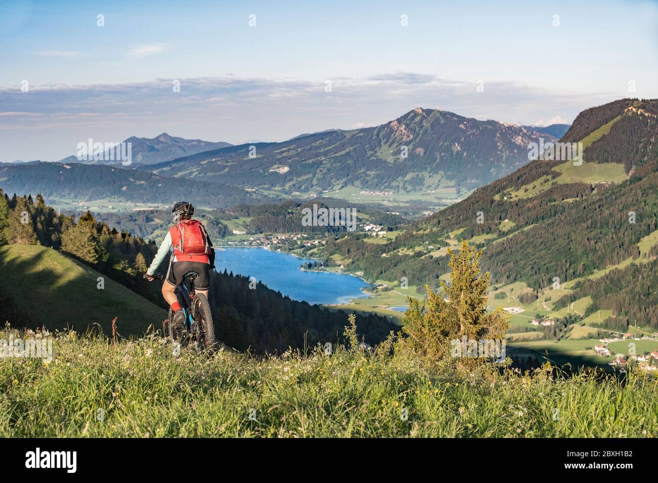 Hübsche Seniorin auf ihrem Elektro-Mountainbike in warmen Morgenstunden Sonnenhöhen von Salmas hoch über Oberstaufen, mit spektakulärem Blick auf den See A Stockfoto