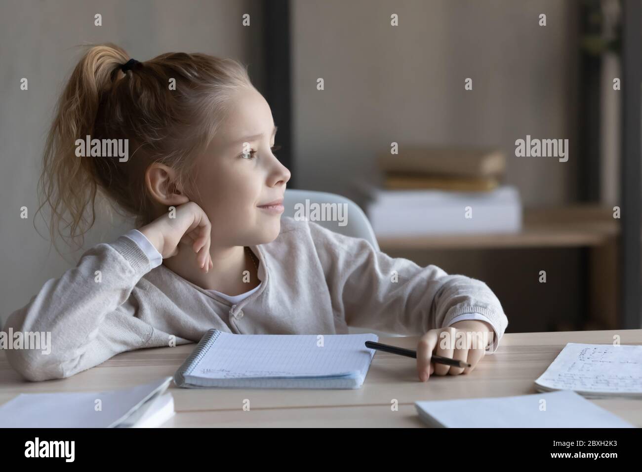 Verträumtes kleines Mädchen abgelenkt vom Studium zu Hause Stockfoto