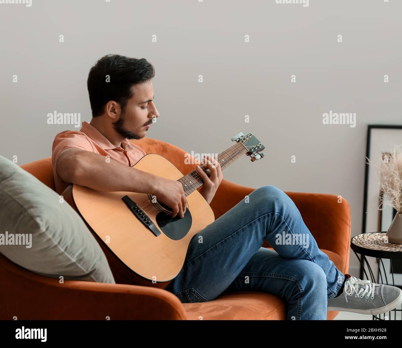 Hübscher junger Mann spielt Gitarre zu Hause Stockfoto
