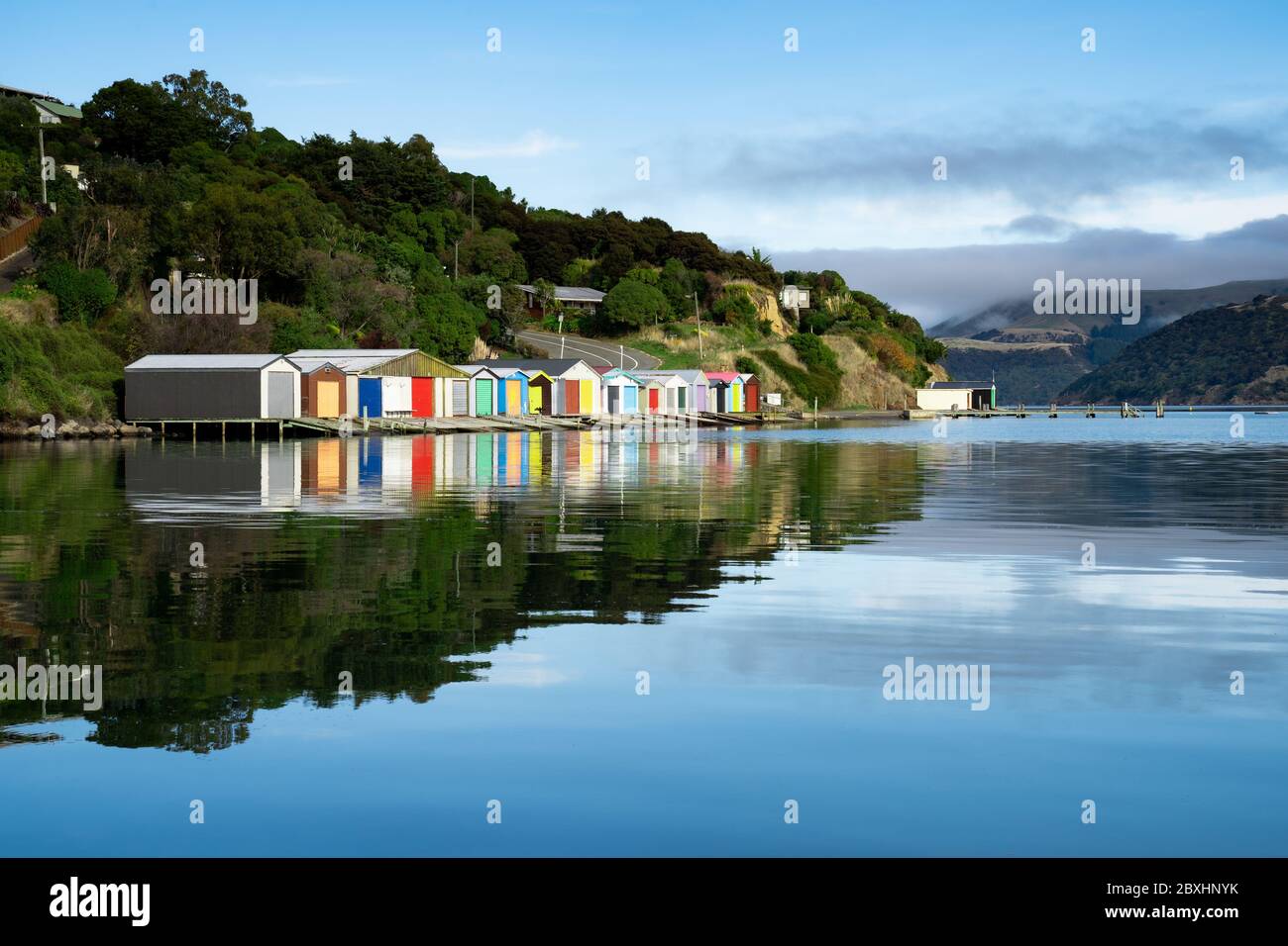 Bunte Bootsschuppen mit schönen Reflektionen am Tag in Duvauchelle, Akaroa Hafen auf Banks Peninsula in South Island, Neuseeland. Stockfoto