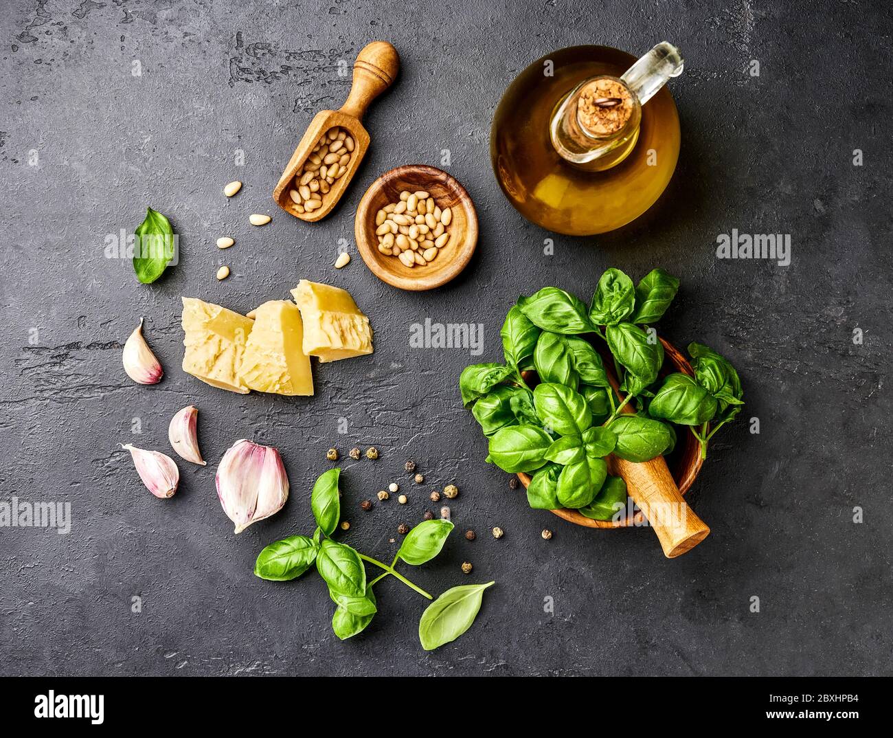 Pesto-Sauce Kochen. Basilikumblätter, Olivenöl, Knoblauch, Pinienkerne und Parmesan. Blick von oben auf den dunklen Steintisch Stockfoto
