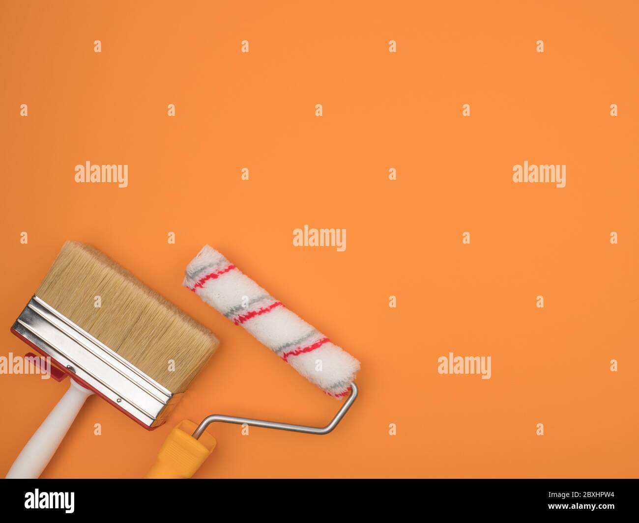 Eine Malrolle und ein großer Pinsel auf einem orangen Hintergrund. Stockfoto