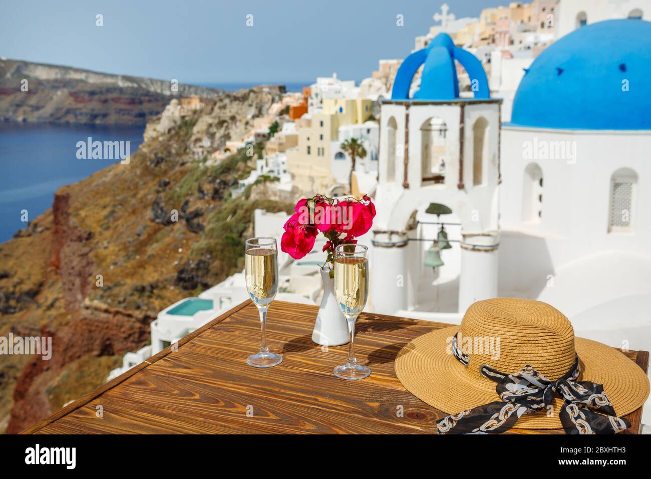 Zwei Gläser Weißwein und ein Hut auf dem Tisch, vor der Kulisse der Insel Santorini Stockfoto