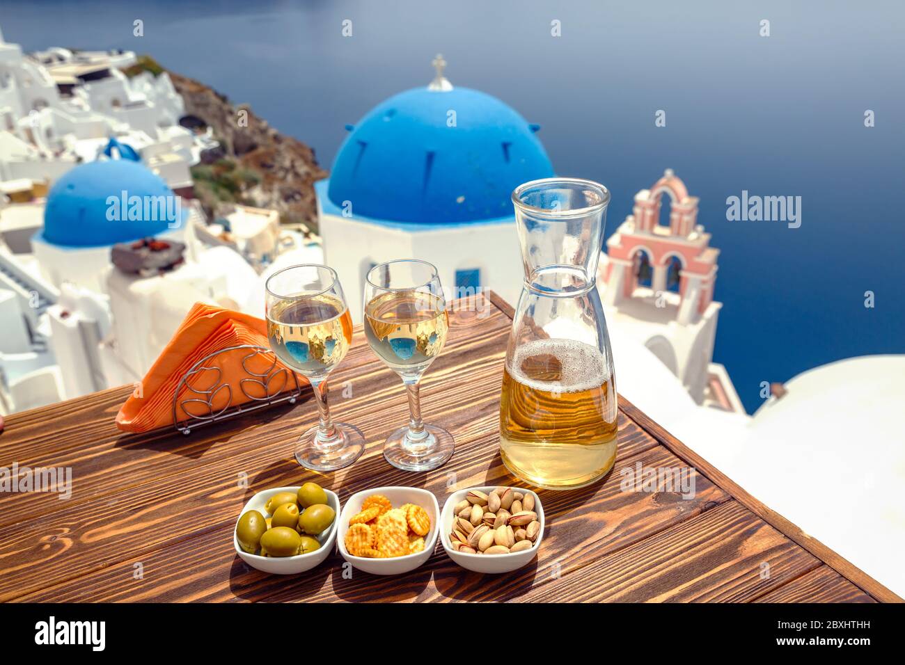 Eine Flasche Wein und zwei Gläser auf dem Tisch, vor der Kulisse der Insel Santorini Stockfoto