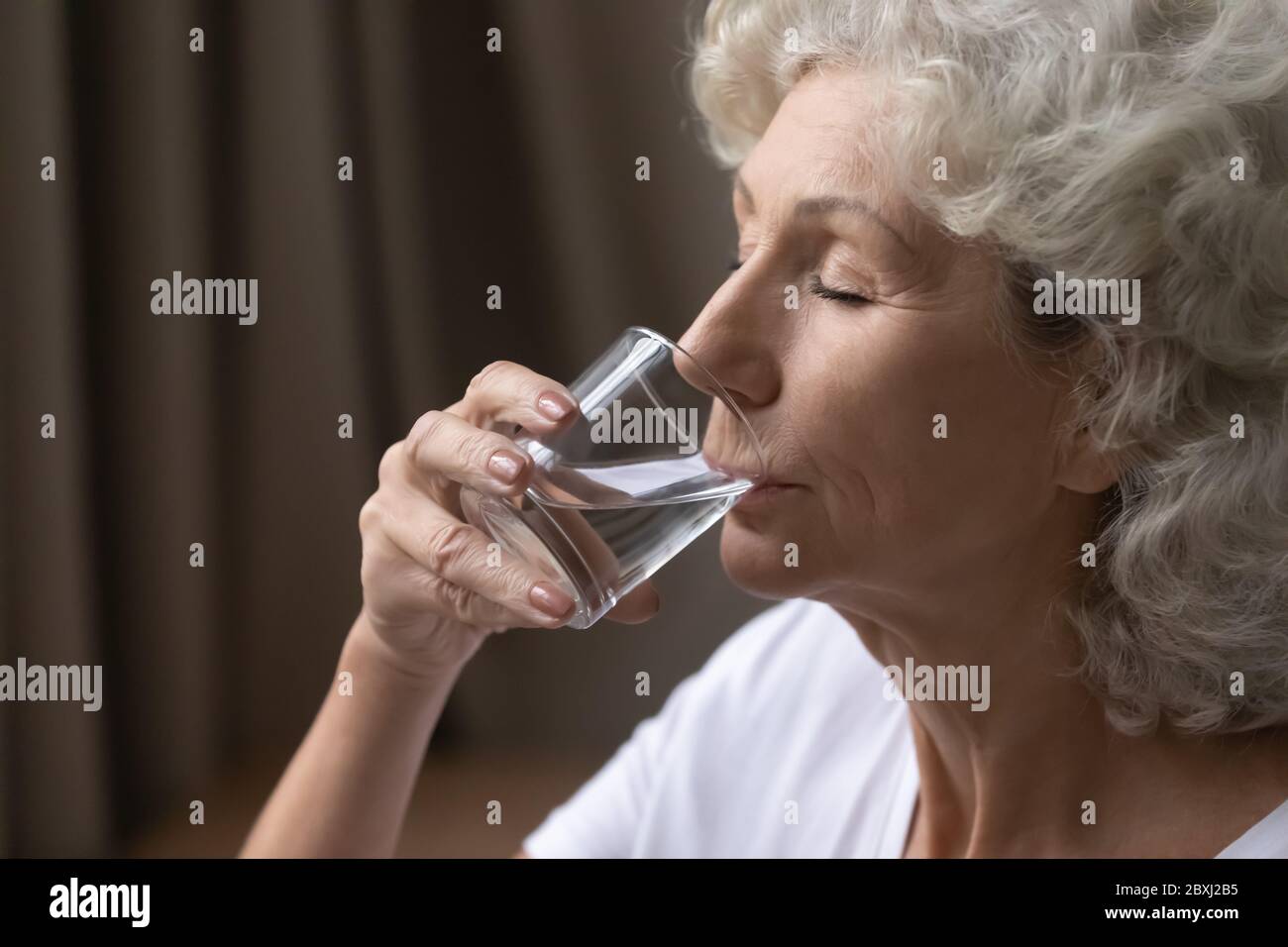 Durstige reife Frau mit einem Glas Wasser Stockfoto
