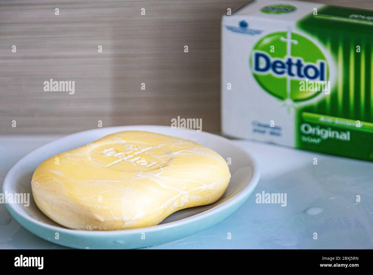 Nahaufnahme des antibakteriellen Dettol Seifenstegs auf einem blauen Seifenhalter auf einem Waschbecken im Bad mit der Schachtel mit Dettol-Logo im Hintergrund. Stockfoto