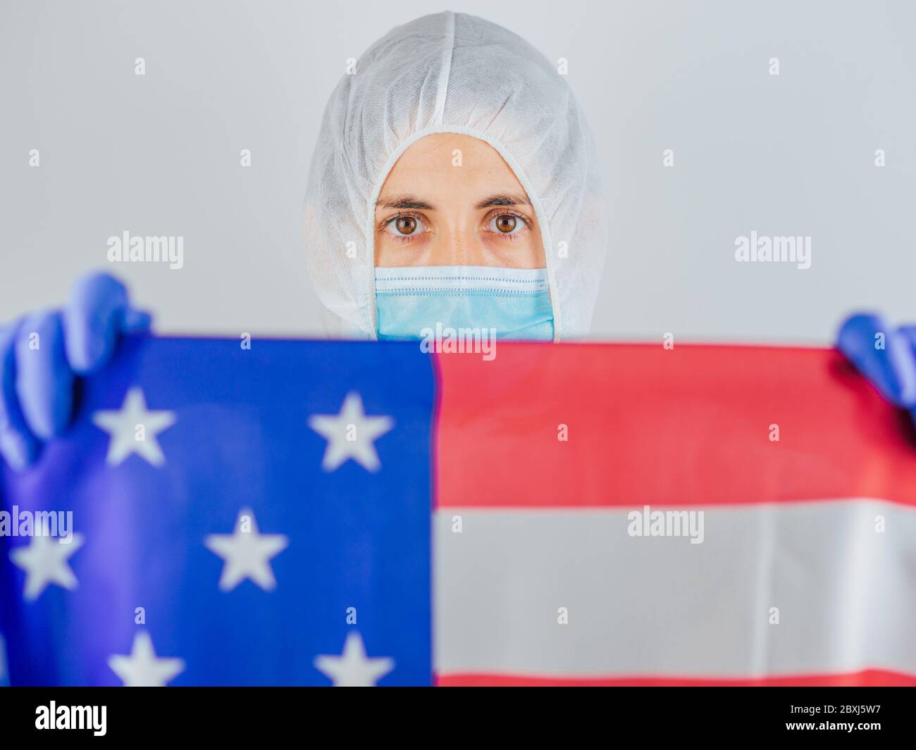 Porträt einer kaukasischen Ärztin mit psa-Anzug und Maske im Krankenhaus. Hält die Flagge der Vereinigten Staaten. Frau vor dem Coronavirus geschützt. Stockfoto