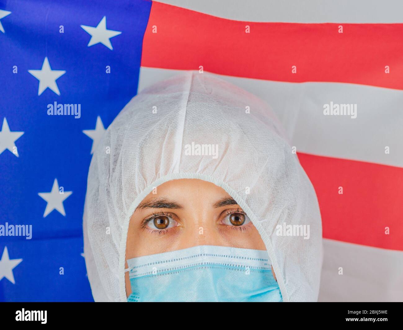 Porträt einer kaukasischen Ärztin mit psa-Anzug und Maske im Krankenhaus. Hält die Flagge der Vereinigten Staaten. Frau vor dem Coronavirus geschützt. Stockfoto