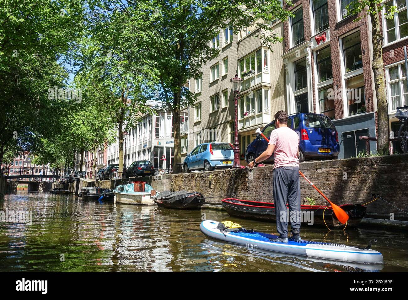 Mann auf einem SUP (Stand-up Paddle Board) auf den Kanälen im Zentrum von Quiet Amsterdam (Niederlande) während der Covid-19-Krise Stockfoto