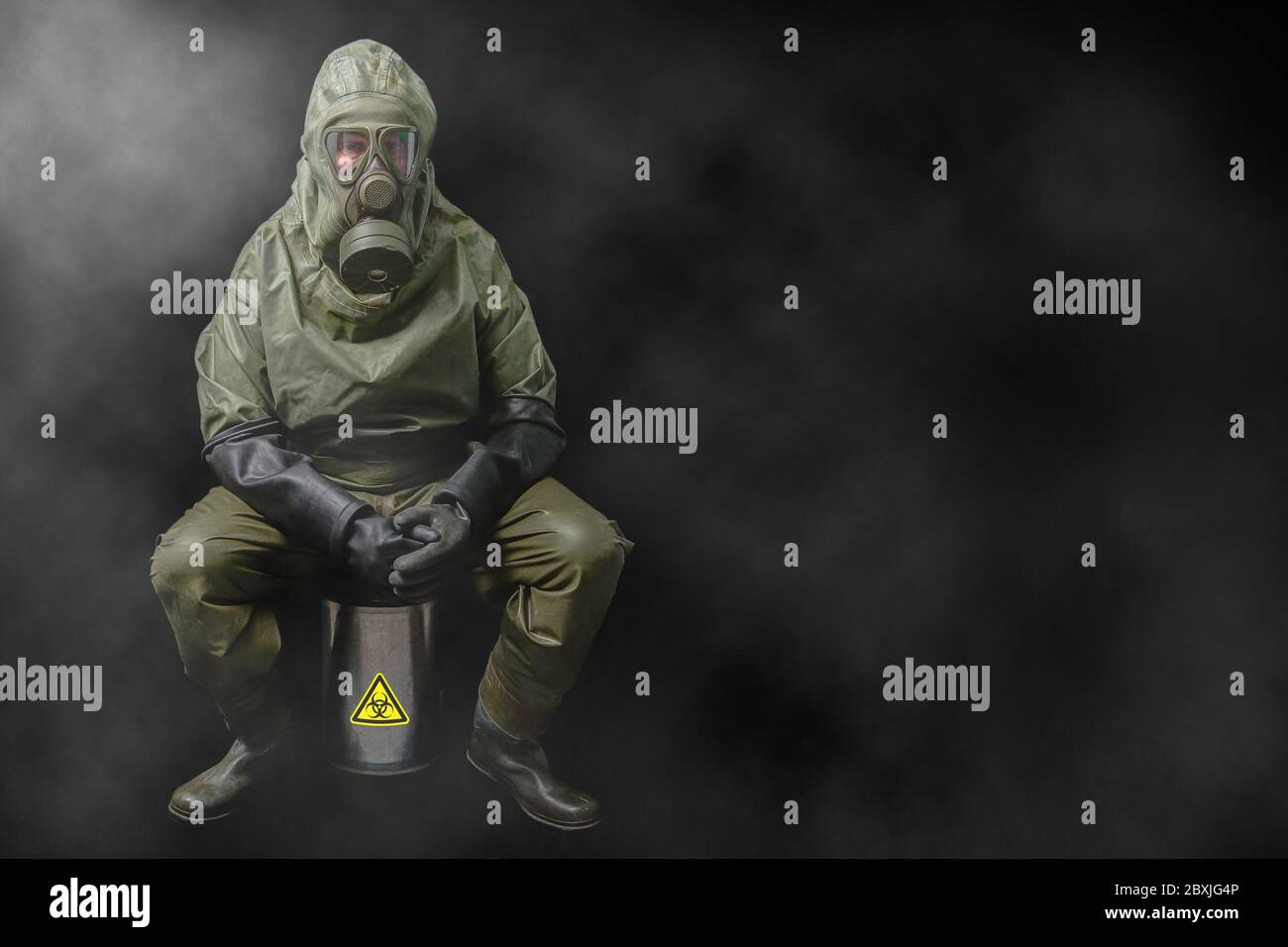 Ein bedrohliches Szenario. Ein Mann in einem NBC-Vollschutzanzug sitzt auf einem speziellen Behälter mit gefährlichen Viren. Stockfoto