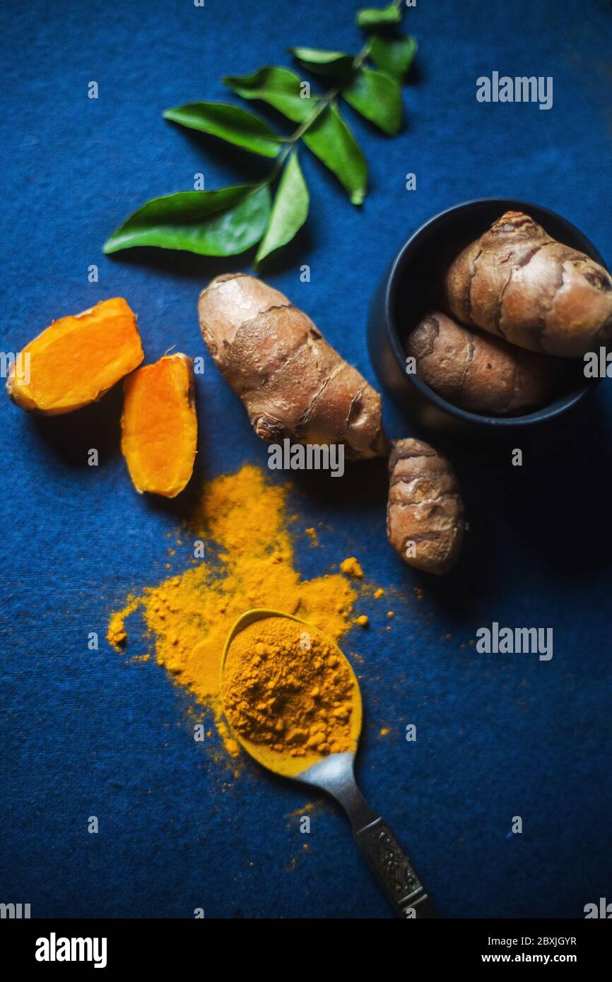 Kurkuma Pulver und Kurkuma Wurzel auf blauem Hintergrund, mit Curryblättern. Blick von oben auf das verheißungsvolle indische Gewürz haldi. Stockfoto