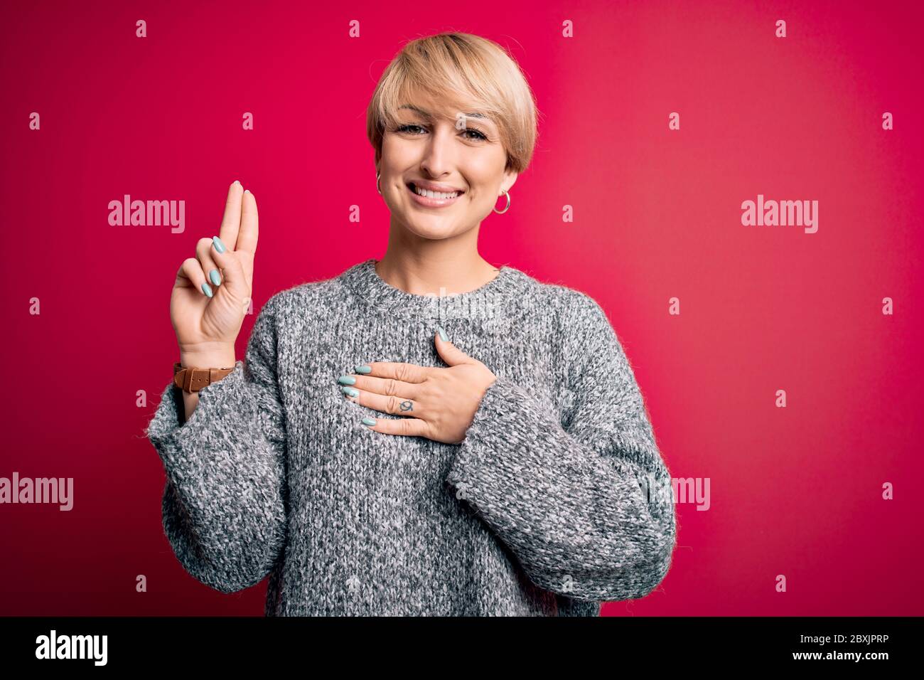 Junge blonde Frau mit modernen kurzen Haaren in lässigen Pullover über rosa Hintergrund lächelnd mit Hand auf der Brust und Finger nach oben, so dass ein loy Stockfoto