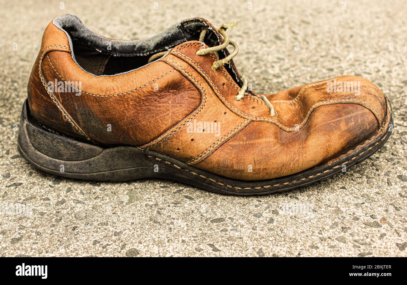 Bequem wie ein alter Schuh, wie das alte Sprichwort sagt. Dieser einfarbige verblasste, abgenutzte, braune Schuh, der auf einem Parkplatz gefunden wurde, scheint seinem Träger gut gedient zu haben Stockfoto