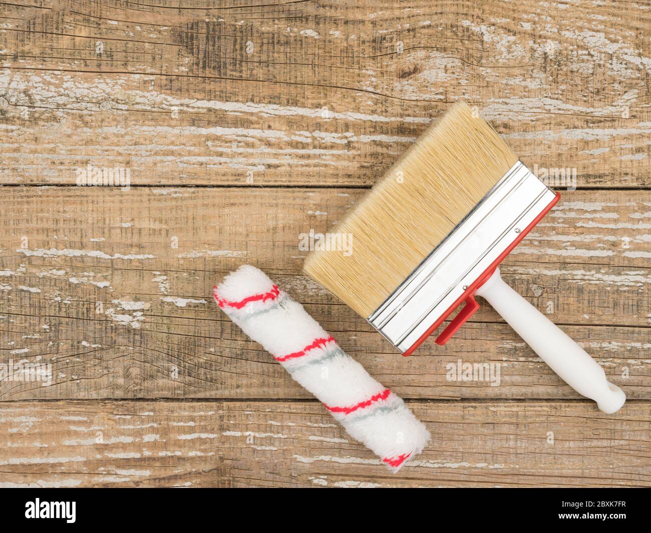 Eine Malrolle und ein großer Pinsel auf einem Holzhintergrund. Stockfoto