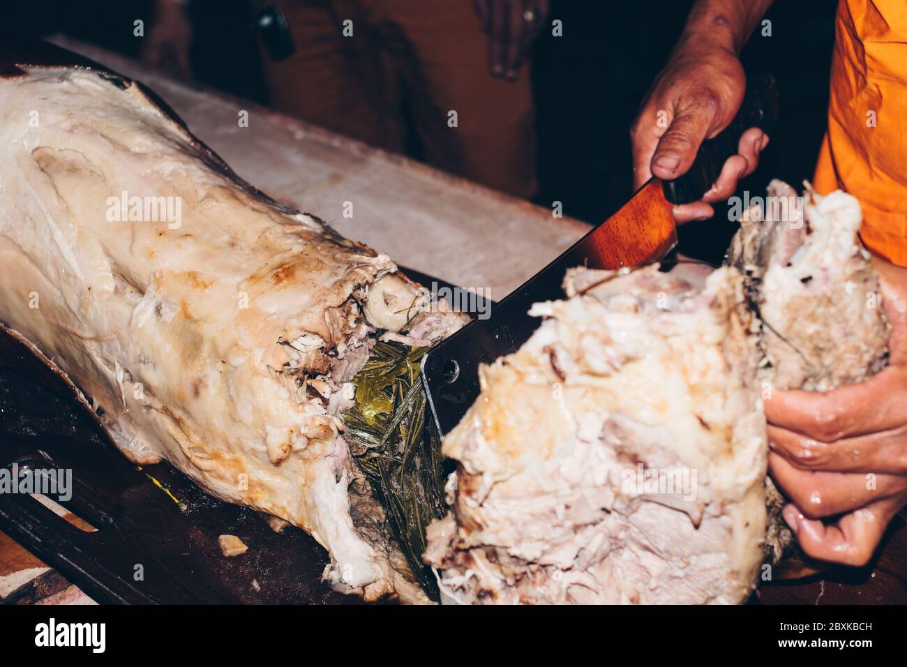 Das gebratene Schwein auf dem Tisch, das als "Lechon" bekannt ist, mit einem Metzgermesser mit der aromatischen Zitronengras-Füllung von Hand schneiden. Selektiver Fokus. Stockfoto