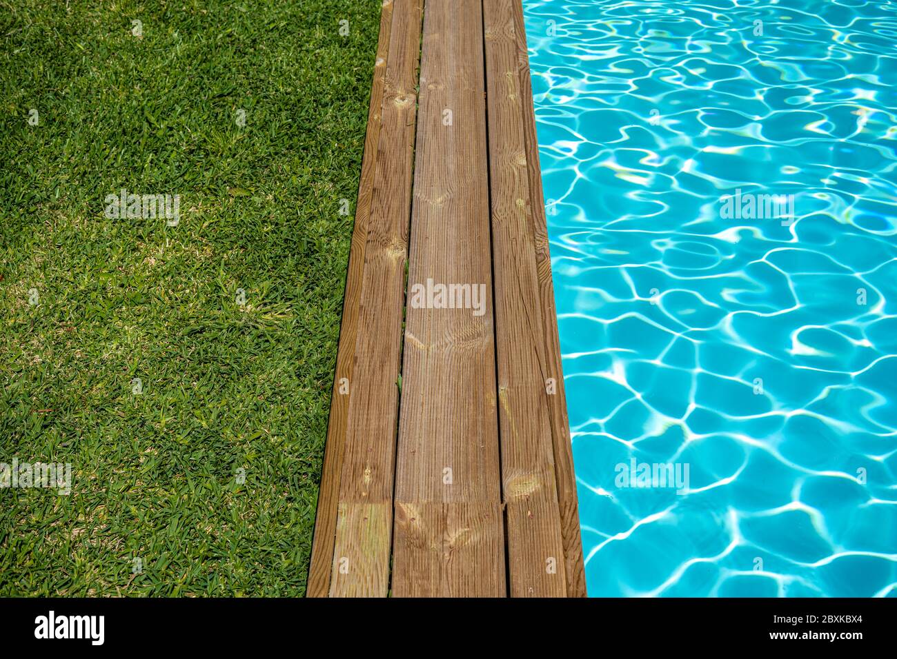 Klares Wasser-Swimmingpool mit Holzterrasse und grünem Gras. Stockfoto