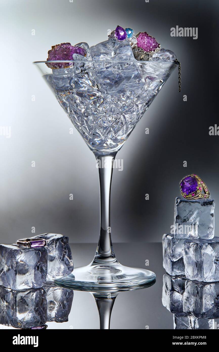 Weißgold Schmuck mit Amethysten und blauem Topas in einem martini-Glas mit  Eis und Eiswürfeln auf grauem Hintergrund mit Spiegelung. Schmuck Kunst und  produ Stockfotografie - Alamy