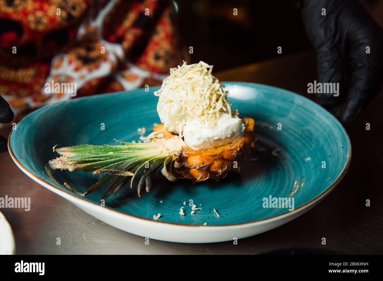 Frisch zubereiteter Salat liegt in der Ananas, die längs geschnitten und mit geriebenem Käse bestreut wird. Alles sieht sehr appetitlich aus. Stockfoto