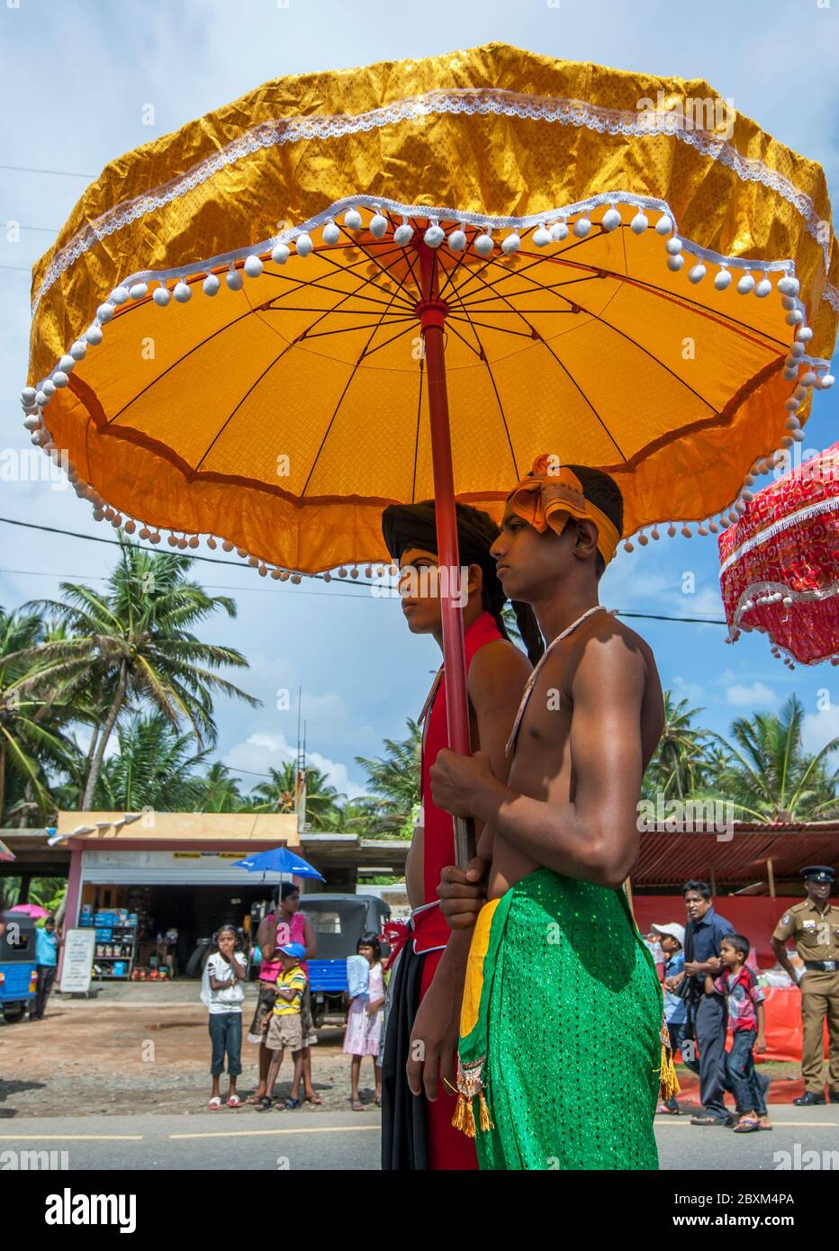 Ein Temple Guardian wird unter einem Schirm von einem Begleiter während Parading entlang der Küstenstraße während einer perahera in Hikkaduwa in Sri Lanka geschützt. Stockfoto