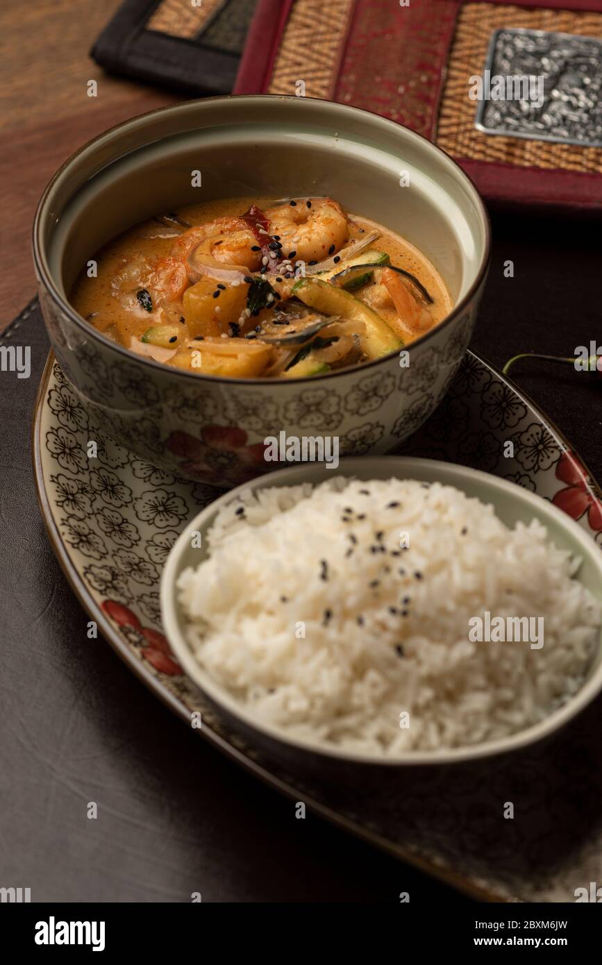 Garnelen mit Curry auf einer Schüssel und Reis auf einer Ledermatte Wodden Tisch Weinglas Stockfoto