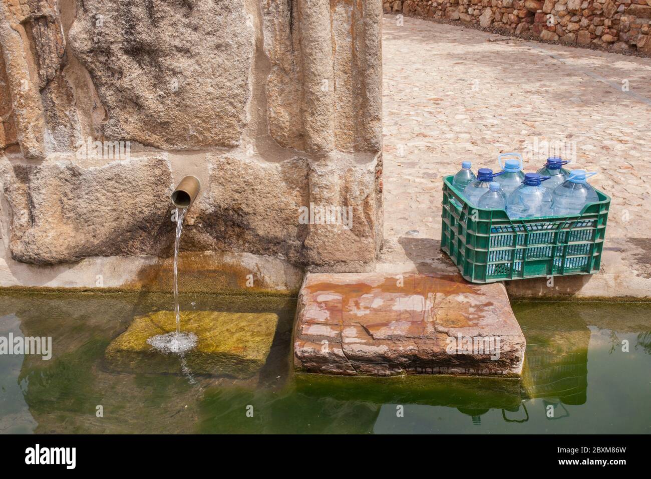 Box voller Flaschen, die am Palomas Pillar Brunnen, Hornachos, Spanien, gefüllt werden können. Kaiserliches Wappen von Carlos V. in der Mitte geschnitzt Stockfoto