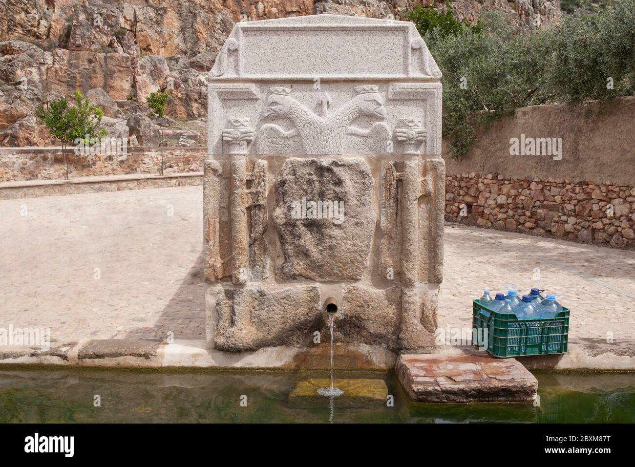 Box voller Flaschen, die am Palomas Pillar Brunnen, Hornachos, Spanien, gefüllt werden können. Kaiserliches Wappen von Carlos V. in der Mitte geschnitzt Stockfoto