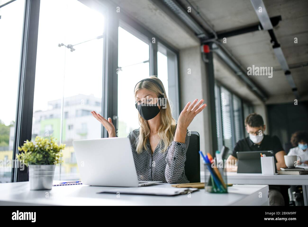 Junge Frau mit Gesichtsmaske zurück bei der Arbeit im Büro nach Lockdown, mit Videoanruf. Stockfoto