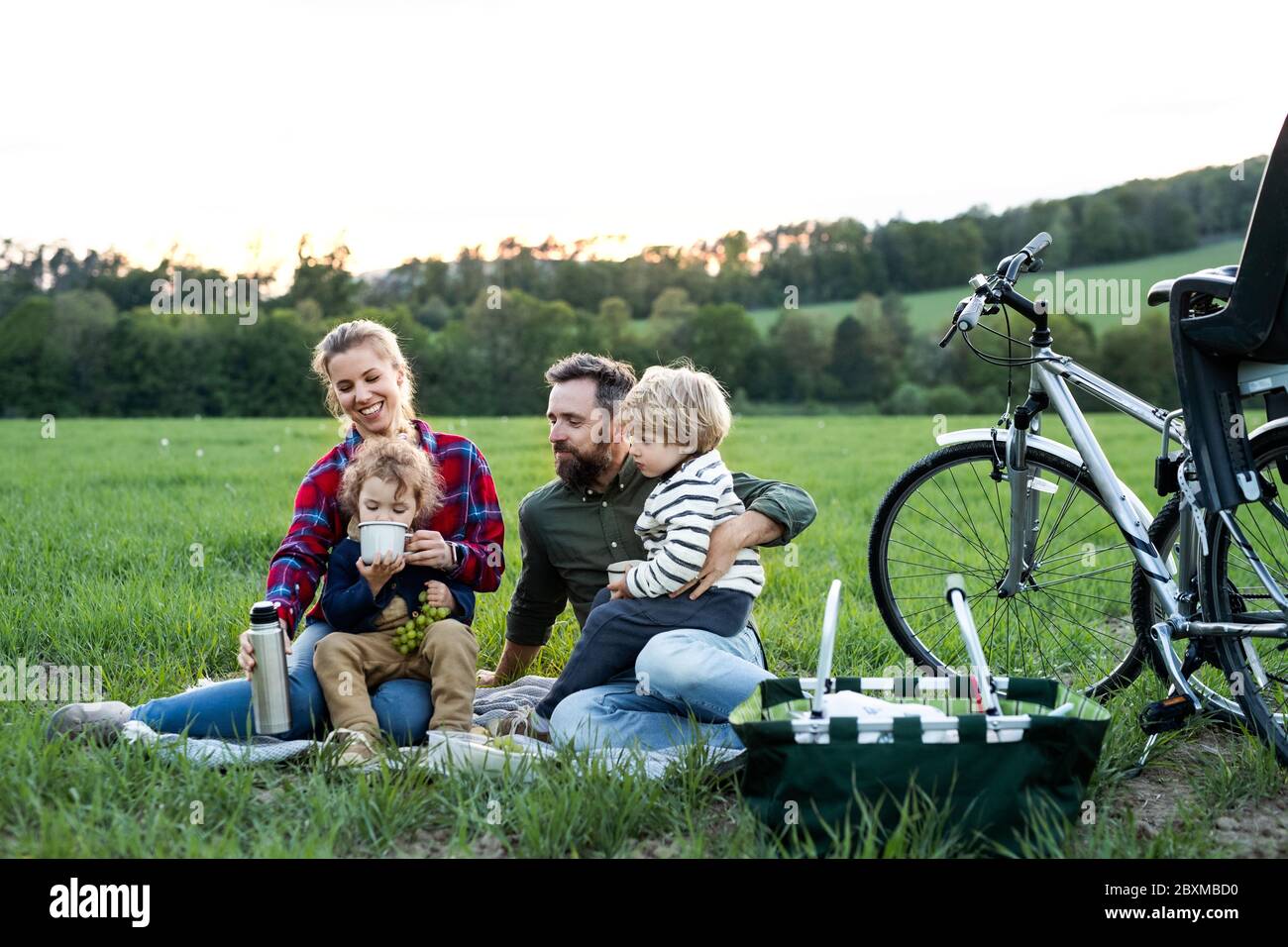 Familie mit zwei kleinen Kindern auf Radtour, auf Gras sitzen und ausruhen. Stockfoto