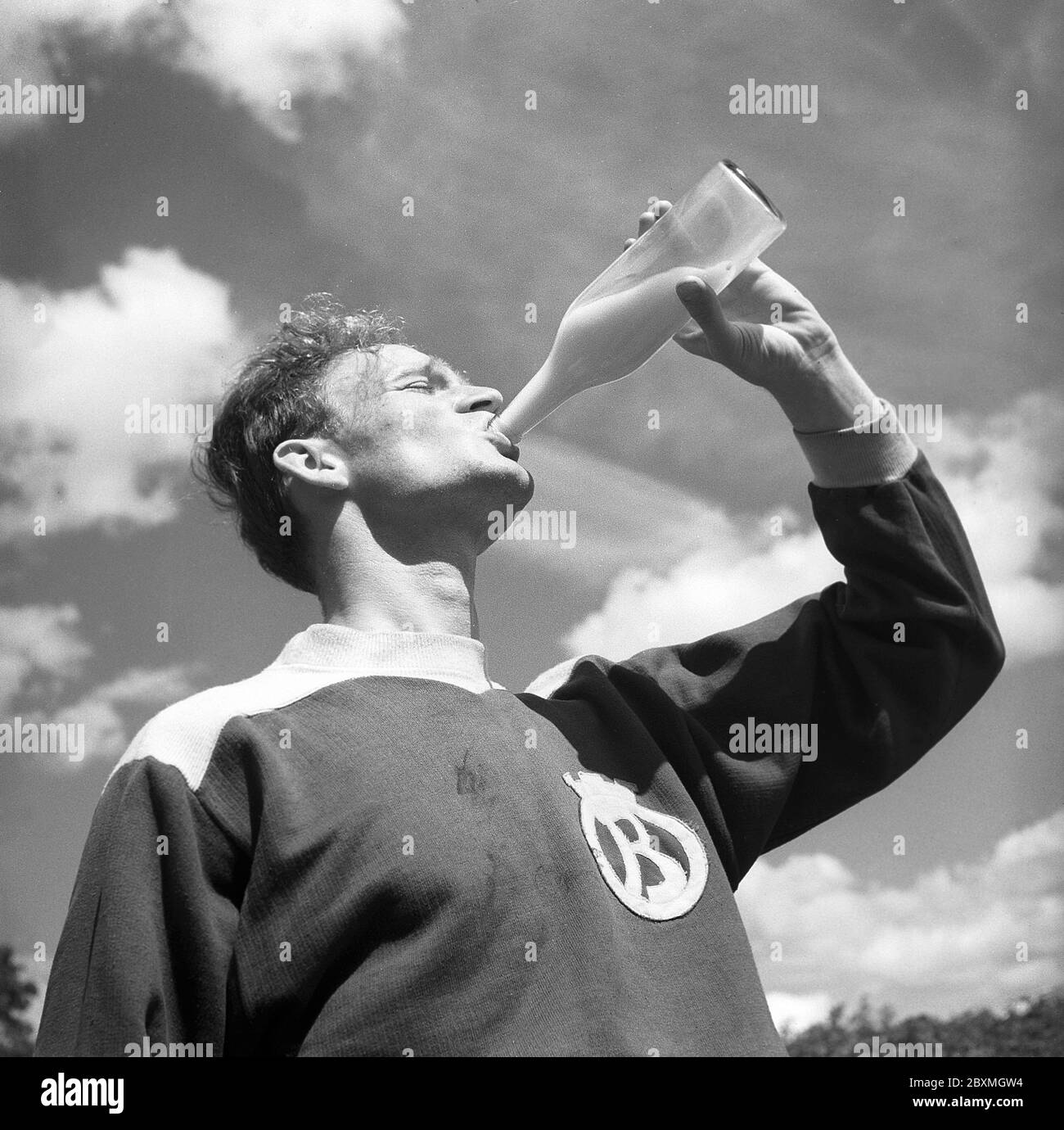 Mann der 1940er Jahre. Athlet Åke Spångert kühlt nach dem Training ab und trinkt aus einer Milchflasche in der Sonne. Zu dieser Zeit wurde Milch verkauft und in Glasflaschen geliefert oder man konnte Milch kaufen, um sie aus dem Laden in der eigenen Flasche nach Hause zu bringen. Schweden juli 1940. 1952 Ref. 145-4 Stockfoto