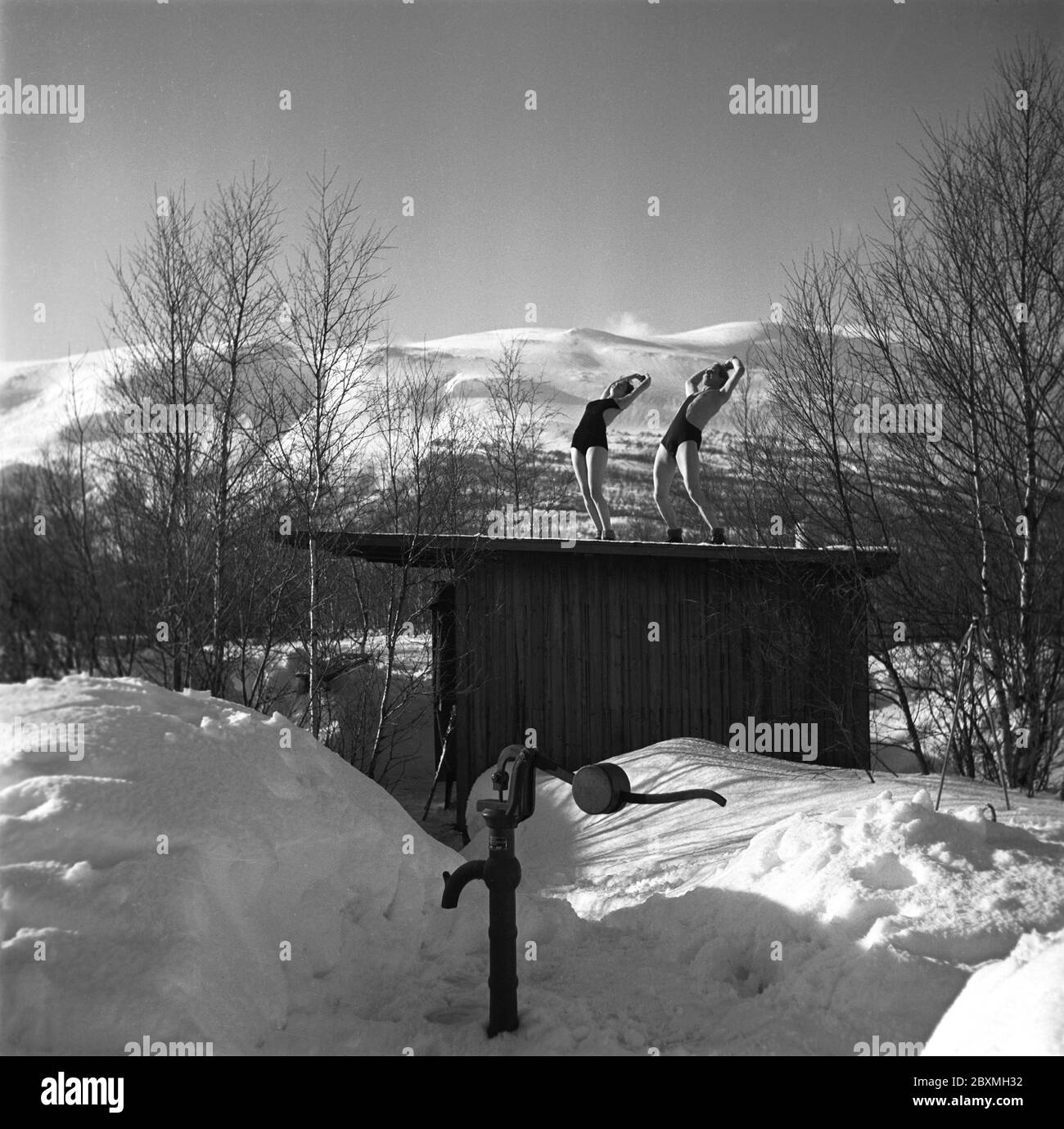 Winter in den 1940er Jahren. Ein junges Paar genießt ihren Winterurlaub in Schwedisch Lappland und trägt ihre Badeanzüge, um sich von der warmen Sonne im Freien zu bräunen. Sie sind auch gesund und gesund während ihrer Winter / Frühling Urlaub und machen Übungen auf einem kleinen Haus. Schweden 1943. Kristoffersson Ref D111-3 Stockfoto